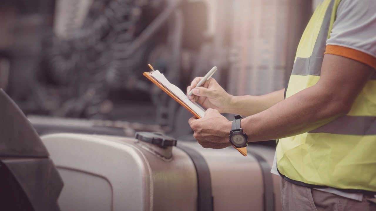 CDL instructor taking notes on a clipboard during truck driver training in the yard